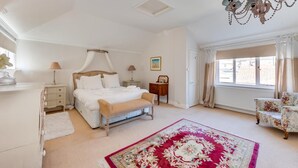A bedroom with a four-poster bed, a chandelier, a floral rug, and a view of the outside through a window. - 1 Bed in Southwold (oc-rest) (Southwold)