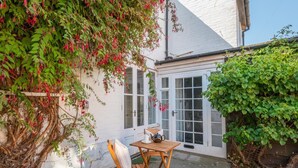 A small patio with a wooden table and chairs, a white door, and a garden wall covered in greenery. - 1 Bed in Southwold (oc-rest) (Southwold)