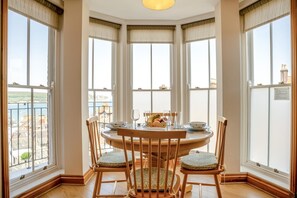 Een zithoek met een ronde tafel, vier stoelen en uitzicht op zee.