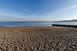 A sandy beach with a wooden pier extending into the water, a clear sky, and a distant hill. - 2 Bed in Swanage (oc-wy514) (Swanage)