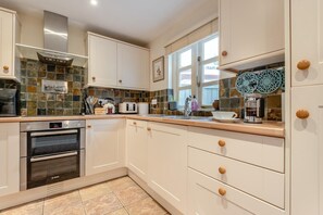 A modern kitchen with white cabinets, a Bosch oven, a built-in microwave, and a window with decorative tiles.