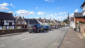 Une rue bordée de maisons traditionnelles à colombages, un clocher d’église et des voitures garées.