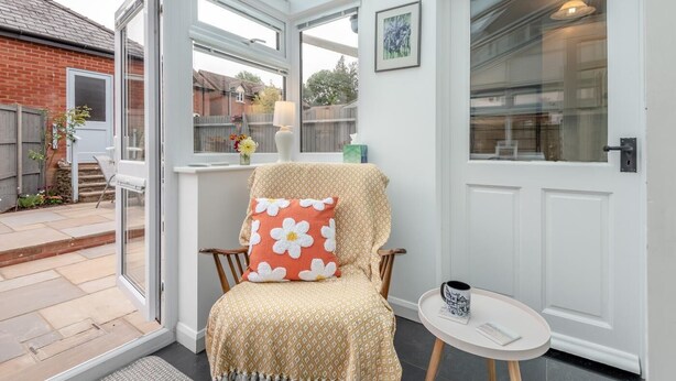 Une véranda équipée d’une chaise, d’une petite table et d’une porte donnant sur un jardin.