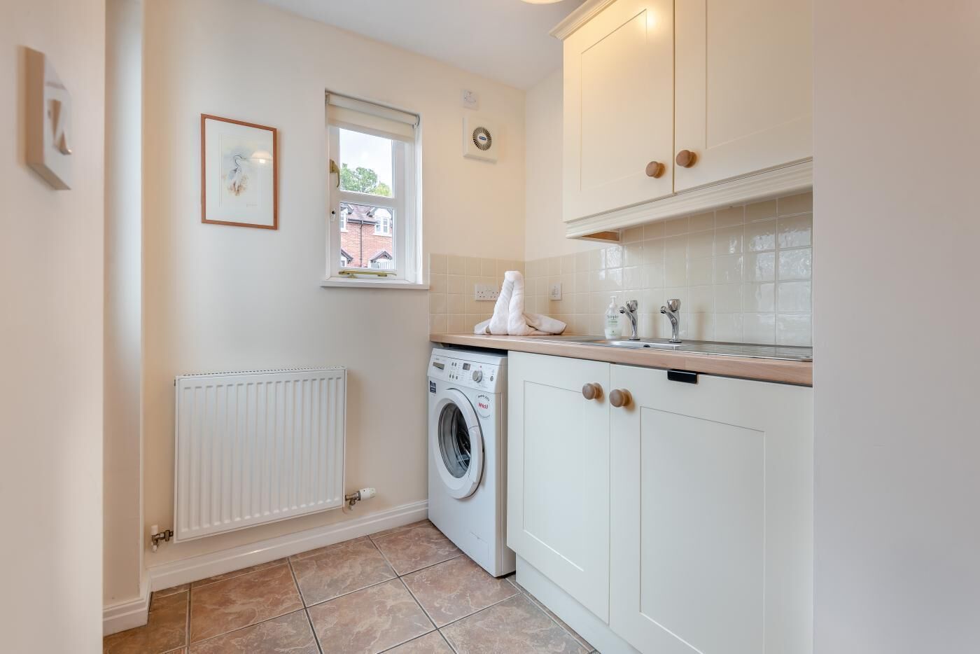 A compact laundry room with a washing machine, a radiator, and a window.