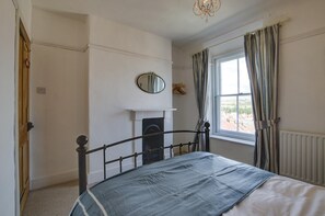 A bedroom with a bed, a fireplace, a window with curtains, and a chandelier. - 2 Bed in Swanage (oc-wy465) (Swanage)
