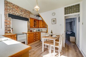 A kitchen with wooden cabinets, a brick wall, a dining table with chairs, and a microwave. - 2 Bed in Swanage (oc-wy465) (Swanage)