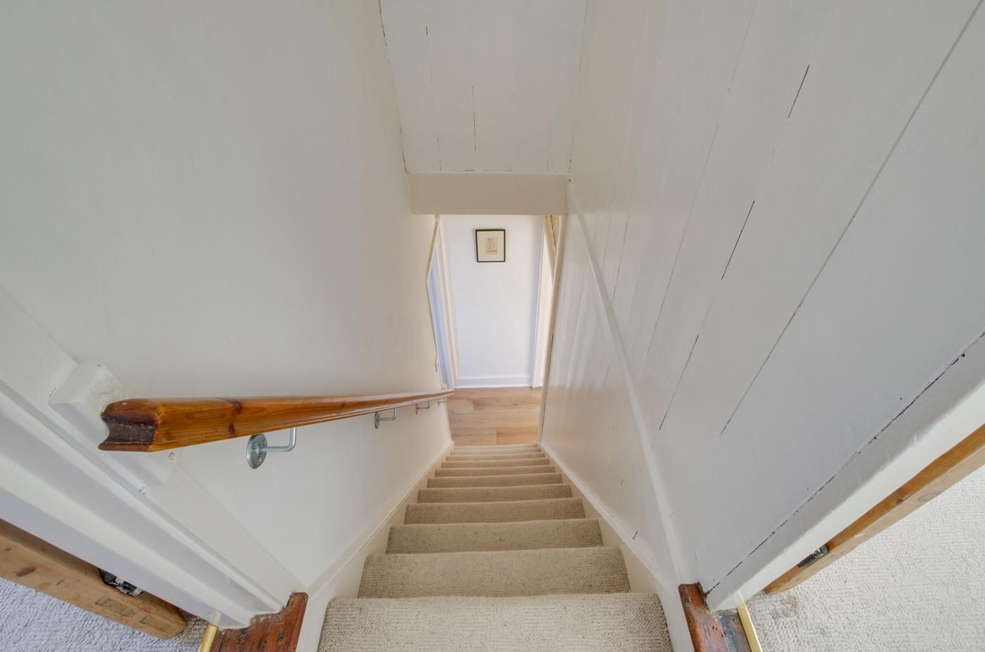 A staircase with a wooden handrail, carpeted steps, and a picture on the wall at the top.