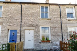 A stone building with a blue door, a white door with the number 225, and a window with plants. - 2 Bed in Swanage (oc-wy465) (Swanage)