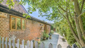 A brick house with a wooden fence, a paved pathway, and a dog sitting on the path. - 1 Bed in Oulton (oc-a32857) (Lowestoft)
