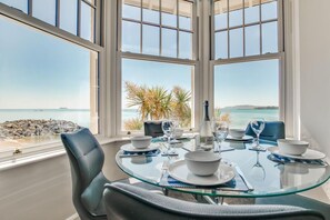 Comedor con mesa y sillas de vidrio, frente a una vista panorámica del océano a través de amplias ventanas.