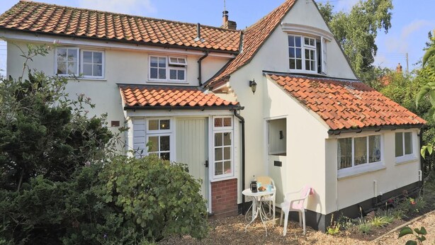 A two-story house with a tiled roof, a small porch, and a garden area with plants and a chair. - 3 Bed in Leiston (oc-wil) (East Bridge)
