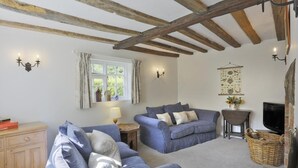 A cozy living room with two blue sofas, a wooden cabinet, a small table with a lamp, and a wall-mounted TV. - 3 Bed in Leiston (oc-wil) (East Bridge)