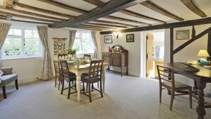 A dining room with a wooden table set for four, flanked by chairs. A wooden cabinet with a mirror and a telephone is against the wall. - 3 Bed in Leiston (oc-wil) (East Bridge)