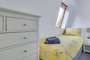 Ein Schlafzimmer mit einem Bett, einer weißen Kommode, einem Fenster und einem Nachttisch.