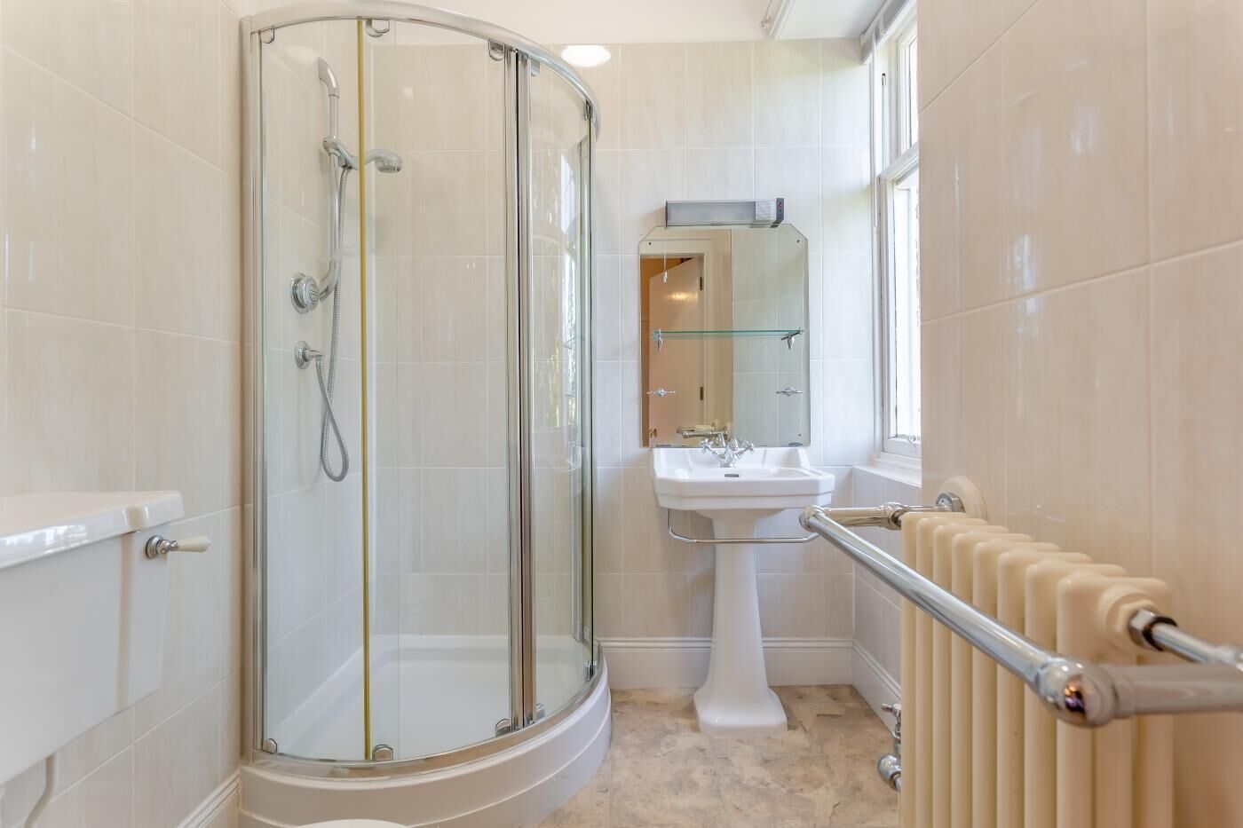 Un baño moderno con ducha envuelta en vidrio, lavabo pedestal y retrete.