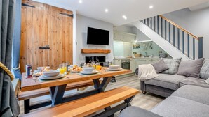A modern living room with a wooden dining table set for breakfast, a grey sofa, and a staircase leading to an upper level. - 3 Bed in Whitby (oc-h33106) (Whitby)