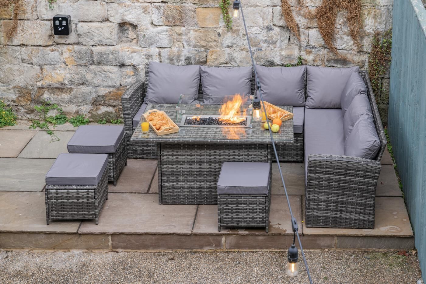A wicker outdoor seating area with a fire feature, a glass table, and a power outlet.