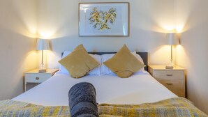 Ein Bett mit zwei Kissen, ein Nachttisch, eine Lampe und ein gerahmtes Kunstwerk an der Wand.