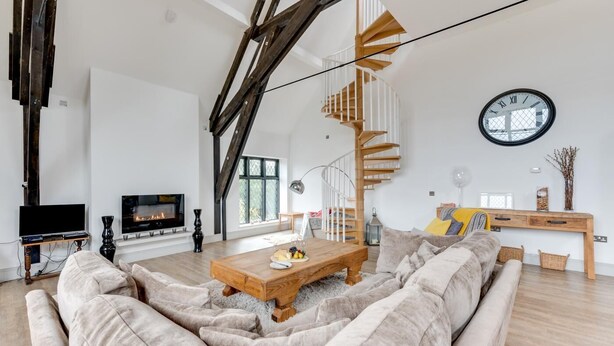 A spacious living room with a large wooden staircase, a fireplace, a television, and a round wall clock. - 4 Bed in Thorpeness (oc-cho) (Thorpeness)