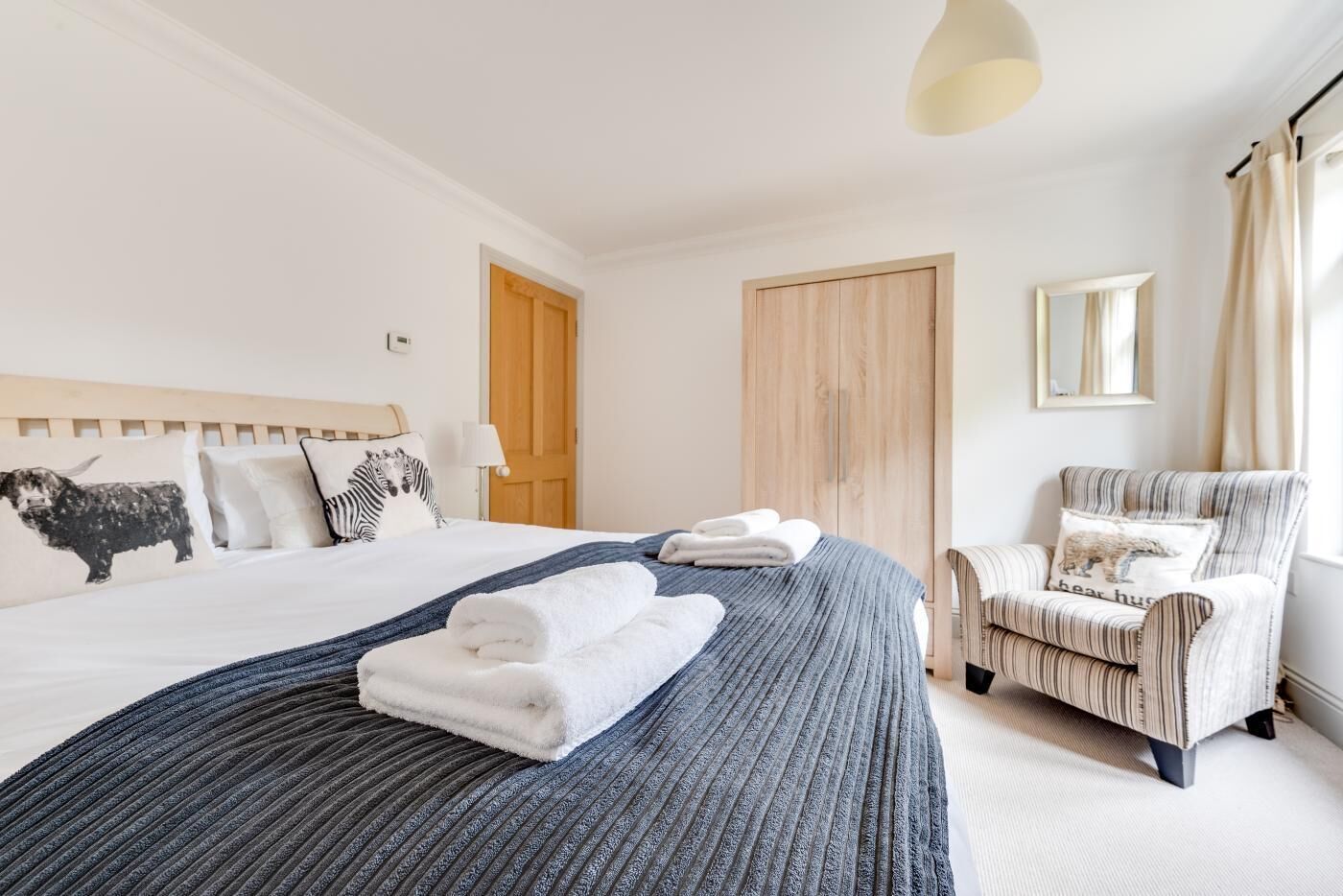 Habitación de hotel con una cama grande, un sillón a rayas, un armario de madera y una ventana con cortinas.