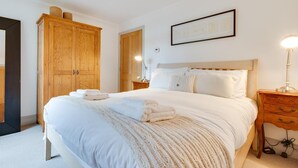 A neatly arranged bedroom with a large bed, wooden wardrobe, and a bedside table with a lamp. - 4 Bed in Thorpeness (oc-cho) (Thorpeness)