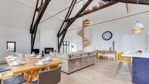 A spacious living area with a wooden dining table set for a meal, a sofa, and a staircase leading to an upper level. - 4 Bed in Thorpeness (oc-cho) (Thorpeness)