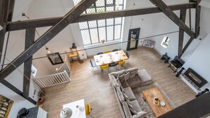 A spacious loft with exposed wooden beams, a dining area with yellow chairs, a grey sofa, and a fireplace. - 4 Bed in Thorpeness (oc-cho) (Thorpeness)