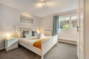 A bedroom with a bed, bedside tables, a radiator, a window with curtains, and a painting on the wall. - 3 Bed in Croyde (oc-f33111) (Croyde)