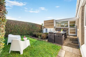 A modern outdoor patio with wicker furniture, a white table, and a glass door leading to a kitchen.