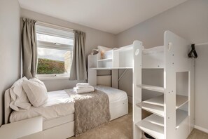 A bedroom with a bunk bed, a window with curtains, a radiator, and a white wardrobe.