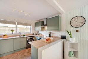 A modern kitchen with a built-in washing machine, a wooden countertop, and a wall-mounted clock.