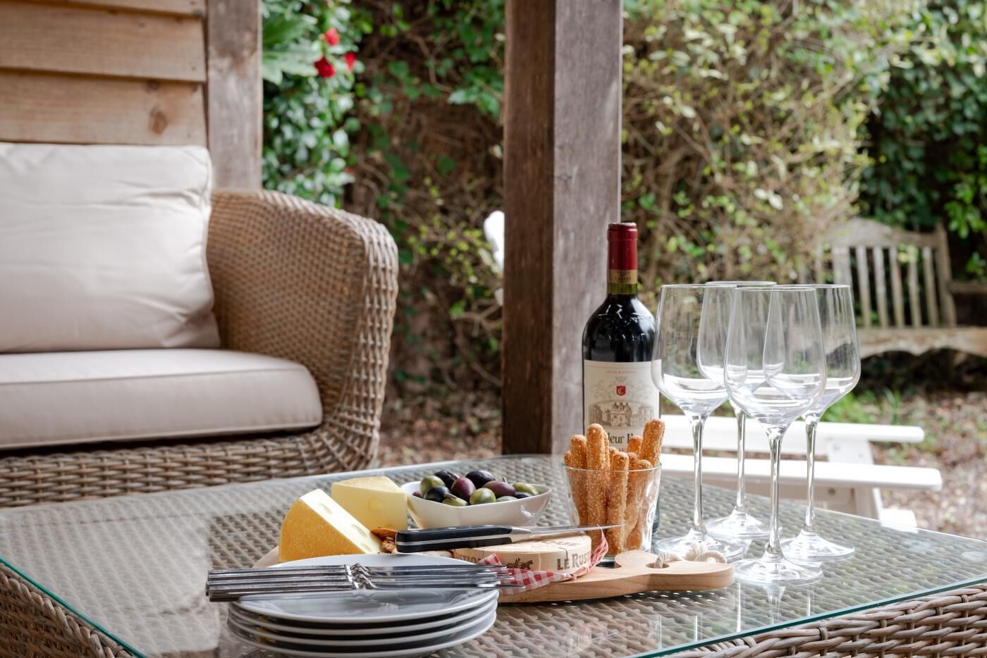 A glass table with a bottle of wine, glasses, cheese, olives, and breadsticks.