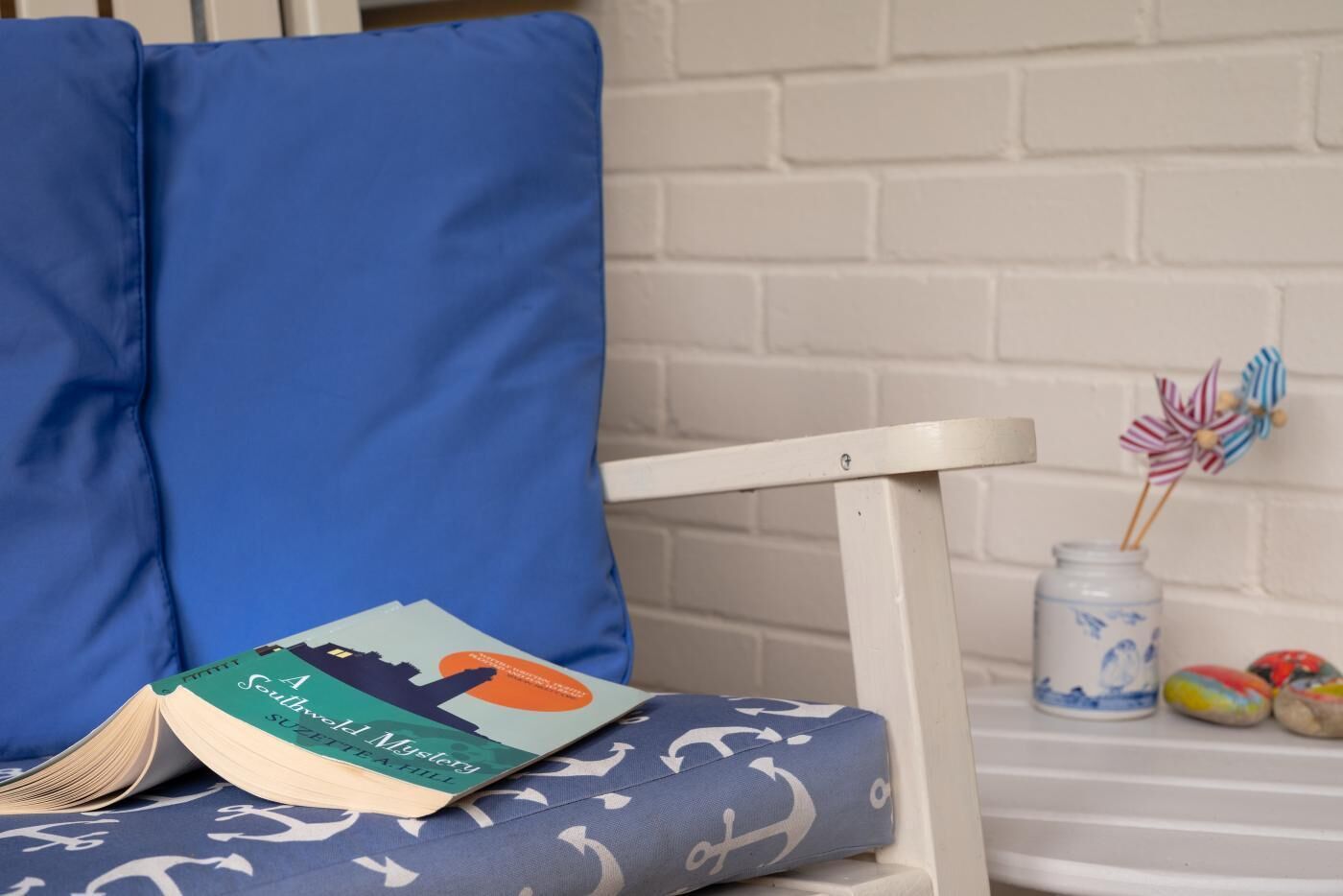 A cozy reading nook with a blue cushioned chair, a small table with a book titled 'A Southern Mystery', and a decorative jar with colorful pins.
