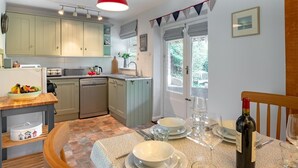 Uma cozinha compacta com armários verde claro, uma luminária pendente vermelha e um espaço de jantar com mesa posta para dois.
