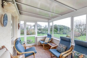 A sunroom with large windows, a wooden table, and blue chairs. - 4 Bed in Worth Matravers (oc-wy115) (Worth Matravers)