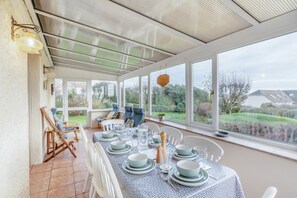 A conservatory with a dining table set for four, large windows, and a view of the garden. - 4 Bed in Worth Matravers (oc-wy115) (Worth Matravers)