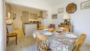 Un coin repas avec une table dressée pour quatre personnes, une cuisine en arrière-plan et un panneau décoratif représentant un navire accroché au mur.