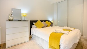 Ein modernes Schlafzimmer mit Bett, Nachttisch, Lampe und einem großen Spiegel.
