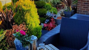 Eine Terrasse mit Frühstückstisch, umgeben von Kübelpflanzen und Blick auf ein Haus.