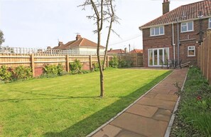 A residential backyard with a lawn, a wooden fence, and a brick house. - 2 Bed in Southwold (oc-deck) (Southwold)