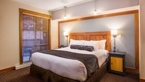 Une chambre d’hôtel avec un grand lit, une tête de lit en bois, deux lampes de chevet, une table de chevet et une fenêtre avec des stores.