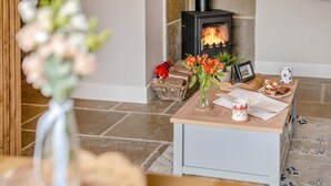 A cozy living room with a fireplace, a wooden table with a vase of flowers, and a basket of bread. - 1 Bed in Askrigg (oc-c33109) (Askrigg)