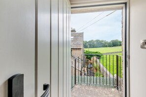 A view from a doorway to a balcony with a metal railing, a grassy field, and a building in the background. - 1 Bed in Askrigg (oc-c33109) (Askrigg)