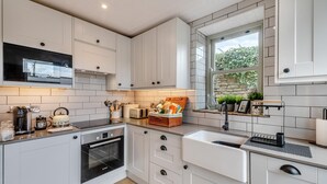 A modern kitchen with white cabinetry, a Bosch oven, a sink, and a window with a view of greenery. - 1 Bed in Askrigg (oc-c33109) (Askrigg)