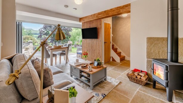 A modern living room with a sofa, coffee table, and a fireplace. There is a dining area with a table and chairs, and a staircase leading to another level. - 1 Bed in Askrigg (oc-c33109) (Askrigg)