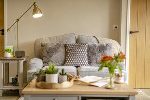 Un salon comprenant un canapé, une table d’appoint avec une lampe et une table basse agrémentée de plantes et de livres.