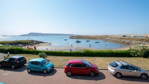 Een parkeerplaats met diverse auto's, een strand en boten op de achtergrond.