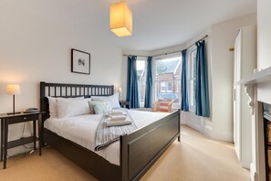 A neatly arranged bedroom with a bed, bedside tables, a lamp, and a view of the outside through large windows. - 4 Bed in Southwold (oc-sl140) (Southwold)