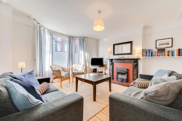 A living room with a fireplace, two armchairs, a sofa, a TV, and a bookshelf. - 4 Bed in Southwold (oc-sl140) (Southwold)