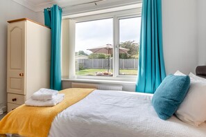 A bedroom with a bed, a wardrobe, a window with curtains, and a view of the outside. - 2 Bed in Reydon (oc-lowrd) (Reydon)